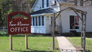 Une enseigne « Two Rivers Office » devant une maison dotée d’un porche et d’un chemin menant à l’entrée.
