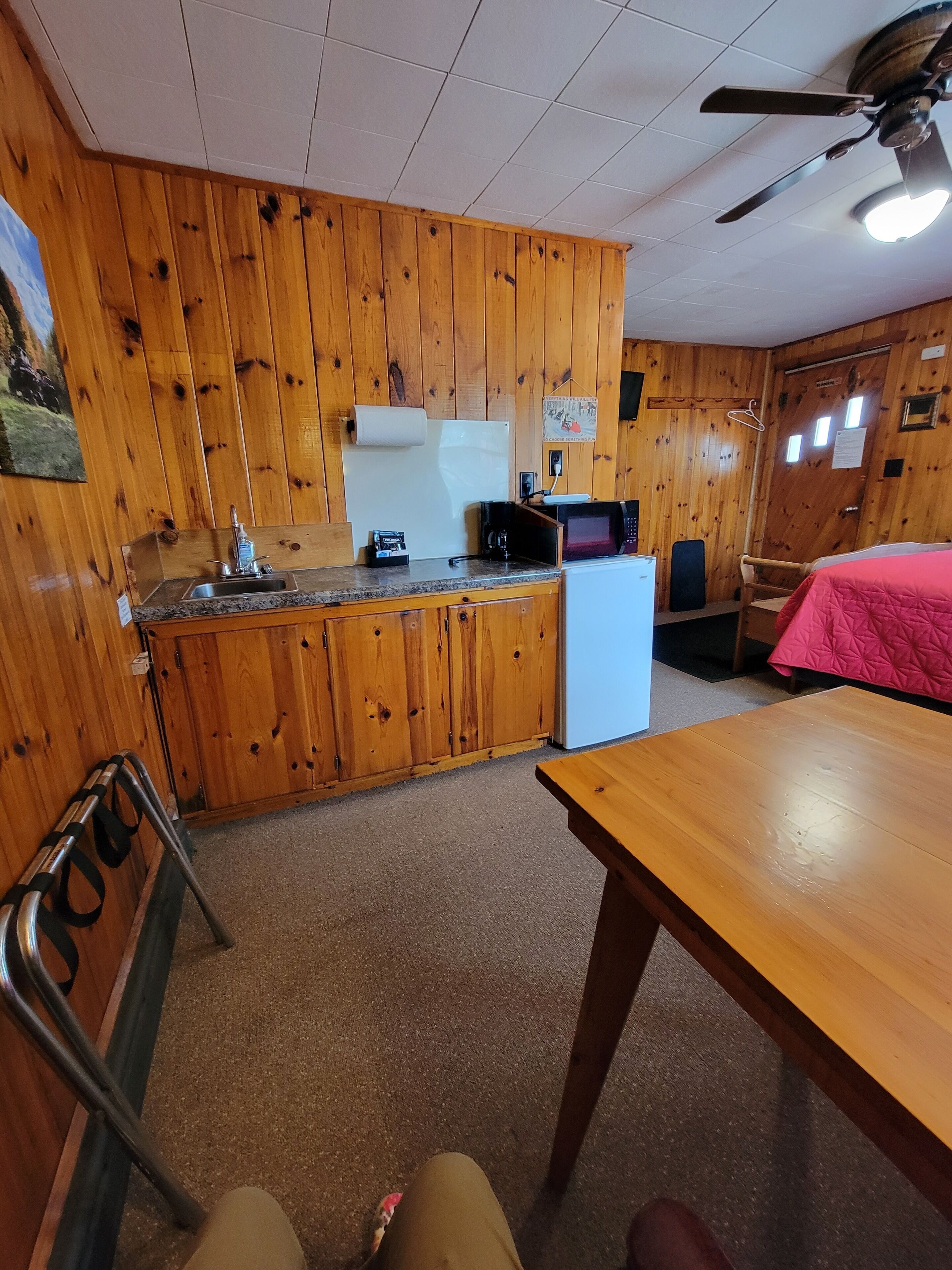 A wooden-paneled room with a kitchen area, including a sink, microwave, and refrigerator.