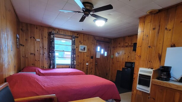 Une pièce aux murs en bois, un lit avec une literie rouge, un ventilateur de plafond, une table avec un menu et une machine à café.