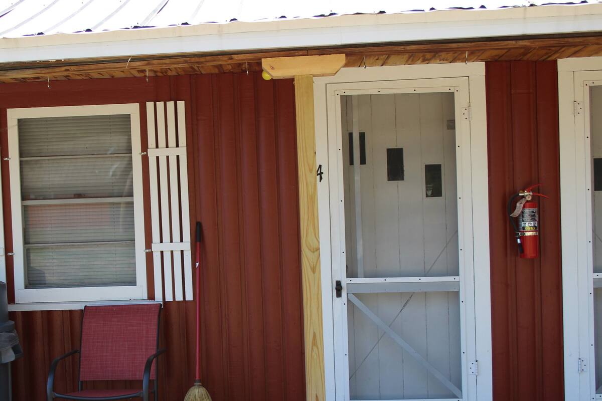 A building with a red exterior, a white door with a screen, a broom, a chair, and a fire extinguisher.