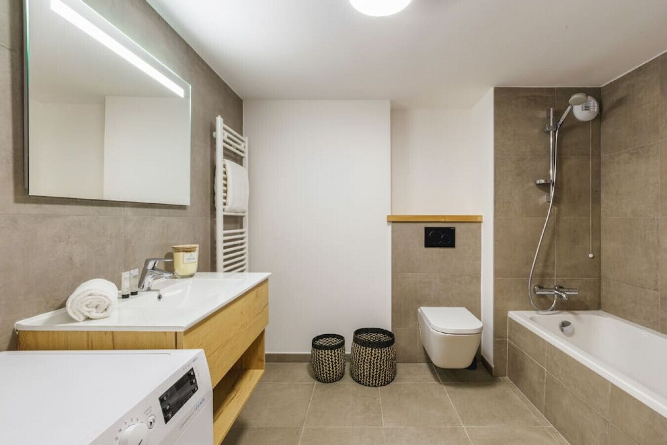 Een moderne badkamer met een wit wastafel, houten wastafelmeubel, toilet en een badkuip met douchekop.