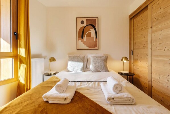 A hotel room with a large bed, two bedside tables with lamps, a wooden wardrobe, and a window with curtains.