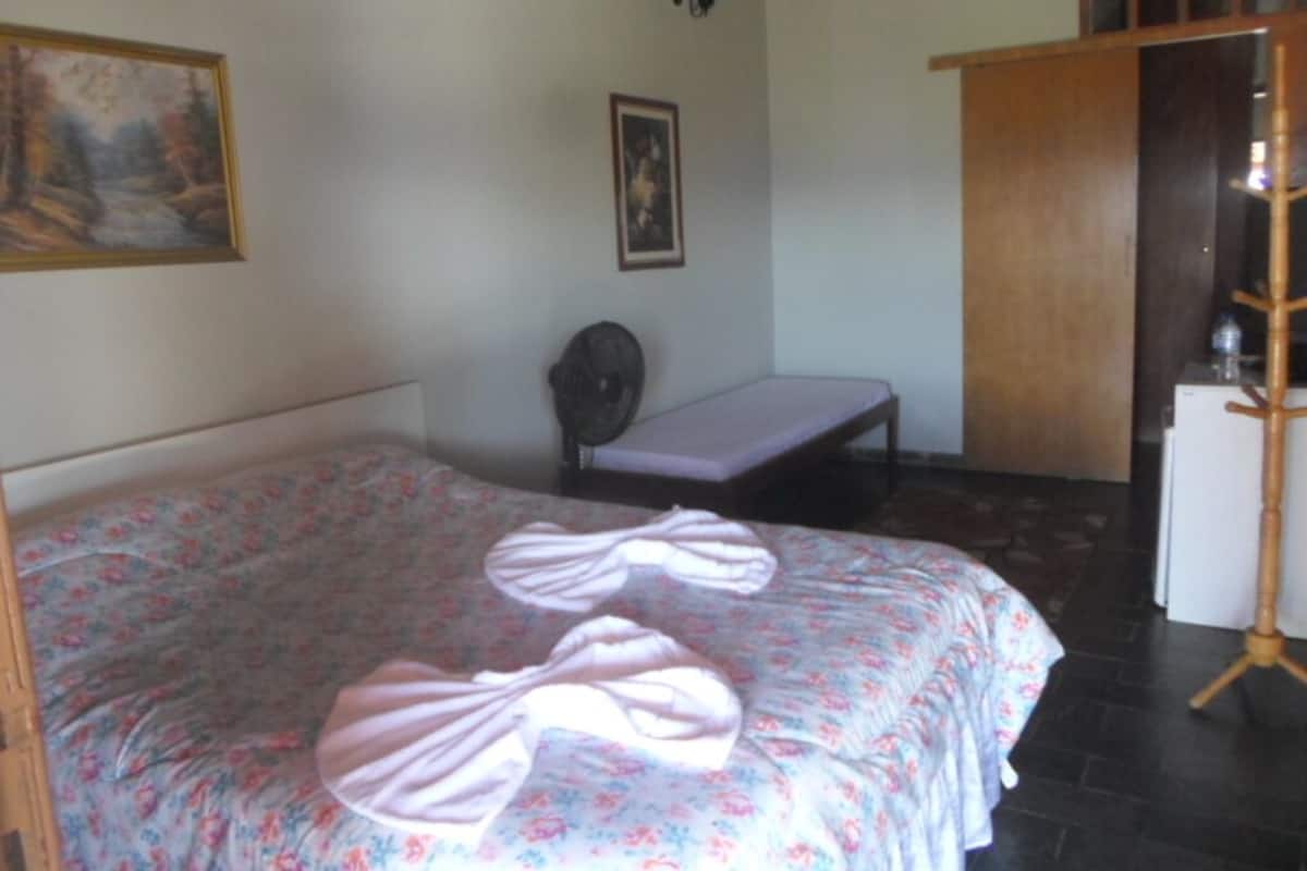 A bedroom with a bed, a chair, a small table, and a wooden cabinet.