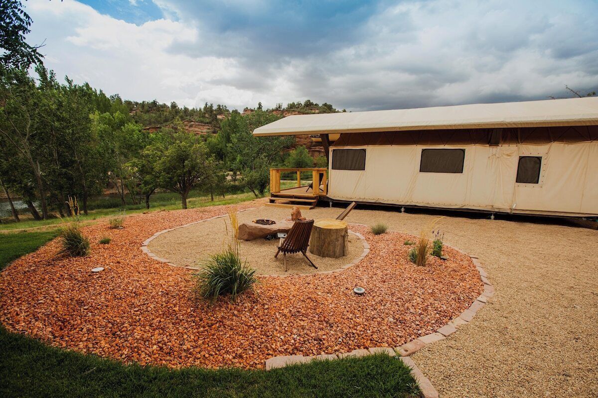 A campsite with a tent, a fire pit, and a seating area surrounded by gravel and small plants.