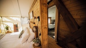 A wooden cabin bedroom with a bed, bedside lamp, and a view of a bathroom. - Cave Lakes Canvas Cabin Suite with Soaker tub #2 (Kanab)