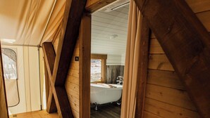 A wooden cabin interior with a sloped ceiling, a wooden floor, and a visible bathroom with a bathtub. - Cave Lakes Canvas Cabin Suite with Soaker tub #2 (Kanab)