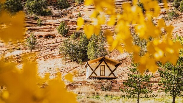 A rustic cabin with a wooden exterior, situated on a rocky terrain with sparse vegetation. - Cave Lakes Canvas Cabin Suite with Soaker tub #2 (Kanab)