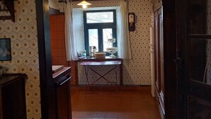 A narrow hallway with a tiled floor, a window with curtains, and a table with dishes. - Charming country house with large barbecue (Gouvy)