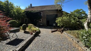 A stone house with a tiled roof, a gravel driveway, and a wooden fence. - Charming country house with large barbecue (Gouvy)