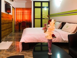 Habitación de hotel con cama, escritorio, silla, un jarrón con flores y televisor montado en la pared.