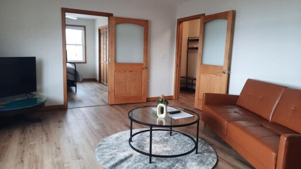 Un salón con una mesa redonda, un sofá, un televisor y puertas de madera que dan a otra habitación.