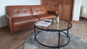 Un sofá de cuero marr ón, una mesa de centro de vidrio y un armario de madera en una habitación con suelo de madera.