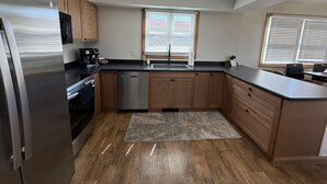Eine moderne Küche mit Holzschränken, einem Edelstahlkühlschrank, einem Geschirrspüler und einem großen Fenster mit Jalousien.