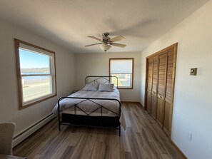A bedroom with a bed, a ceiling fan, wooden flooring, and a view through the window. - Spacious Summer Getaway Ideal for Large Groups (Negaunee)