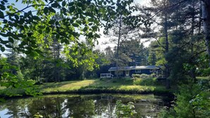 A house by a pond with a grassy area and trees. - Luxury Winter Retreat/Direct Snowmobile Access (Spurr Township)