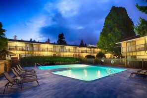 Un hotel con piscina, lettini e facciata ben illuminata al crepuscolo.