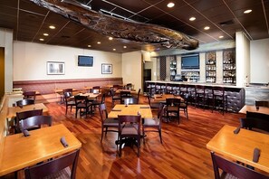 Ein Restaurant mit Holztischen und -stühlen, einer Bar mit Flaschenregalen und einem großen dekorativen Deckengemälde.