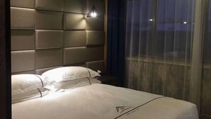 Une chambre d’hôtel avec une tête de lit rembourrée, un lit avec du linge de lit blanc et une fenêtre avec des rideaux.