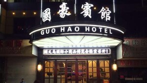 A hotel entrance with a marquee sign, a red carpet, and a person sitting on a bench outside.