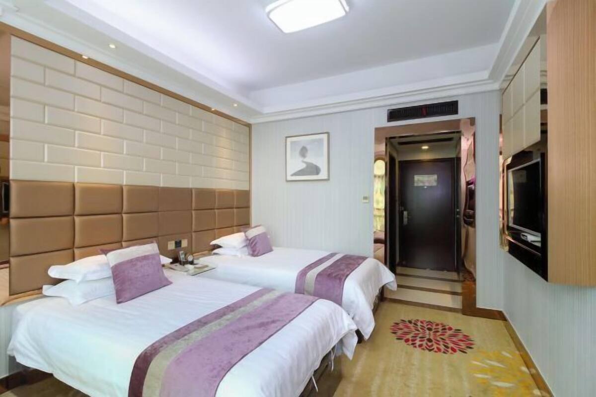 Une chambre d’hôtel avec deux lits, une télévision et un mur décoré d’un motif en briques, ainsi qu’une porte donnant sur une autre pièce.