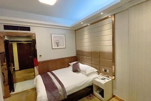 A hotel room with a bed, bedside table, and a mirror.