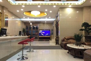 A hotel lobby with a reception desk, a television, a seating area with a sofa and armchairs, and a decorative ceiling light fixture. - Guo Hao Hotel (Yiwu International Trade City) (Yiwu)