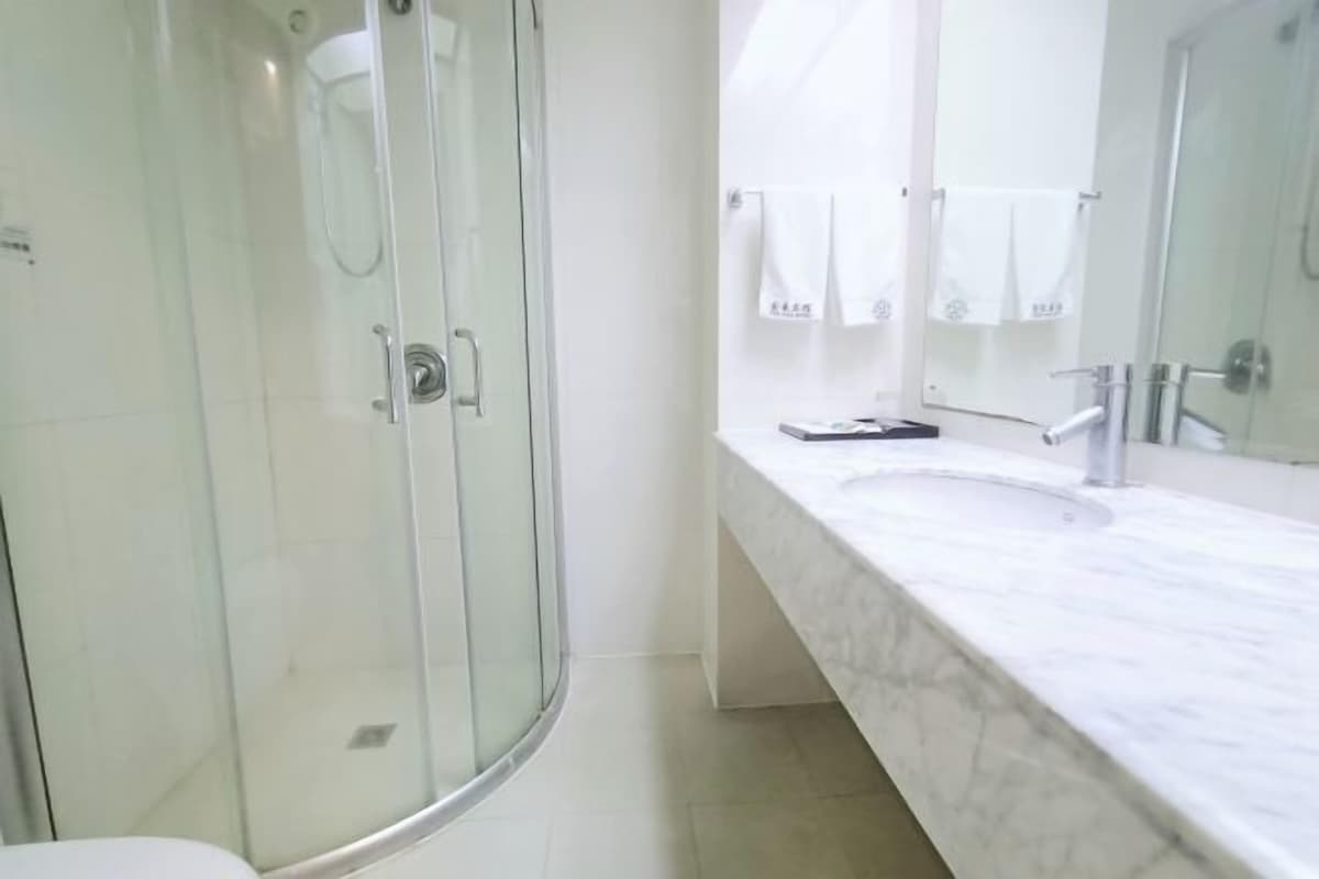 A modern bathroom with a glass shower enclosure, a white sink with a marble countertop, and a large mirror.