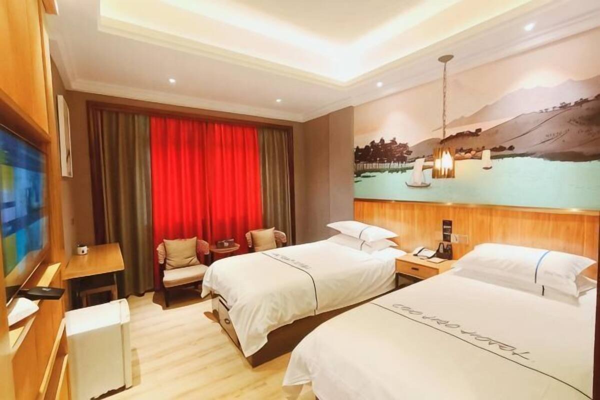 Une chambre d’hôtel avec deux lits, un bureau, une télévision et un tableau représentant un paysage.