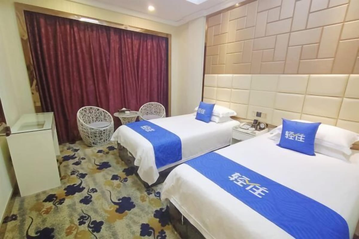 A hotel room with two beds, a small table, two chairs, a desk, and a curtain.