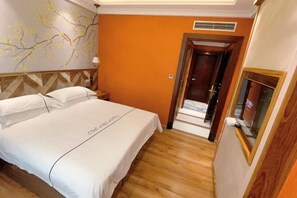 A hotel room with a bed, a nightstand, a wall with a decorative branch pattern, and an orange wall.