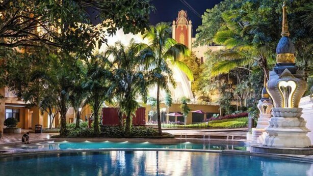 A pool area with a fountain, surrounded by palm trees and a building with a tower in the background. - King Land Hotel (Mengla)
