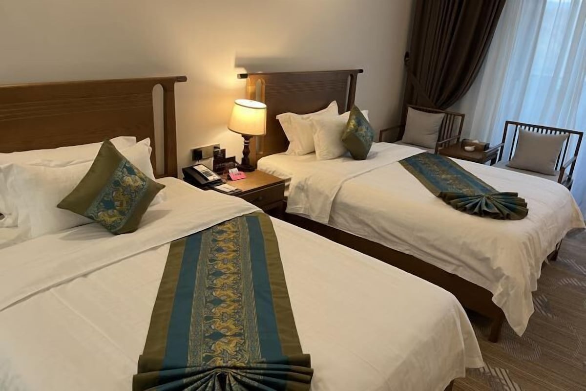 A hotel room with two beds, a nightstand with a lamp, and a chair.