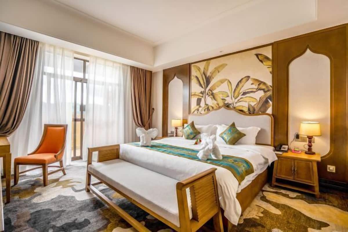 Habitación de hotel con una cama grande, un banco de madera, una silla, una mesita de noche y un cuadro en la pared.