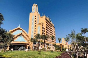 Um hotel com uma imponente torre do relógio, um edifício central espaçoso e um gramado bem cuidado com palmeiras.