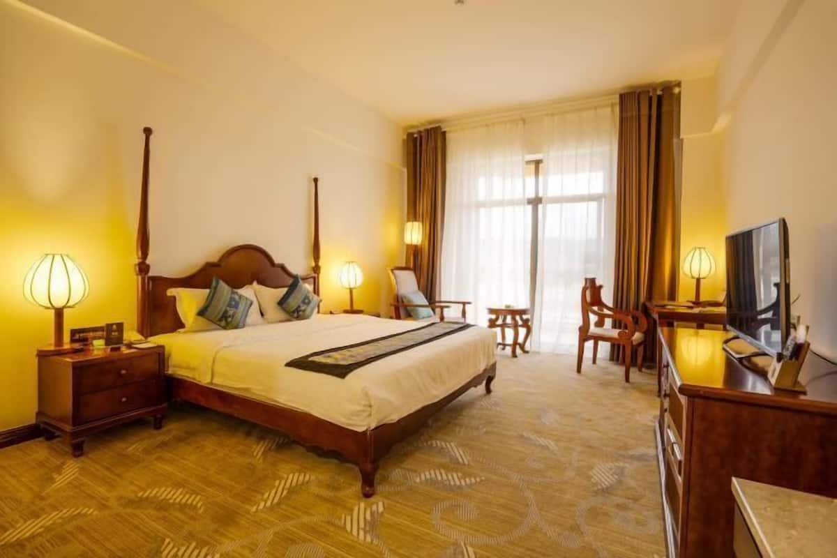 Habitación de hotel con una cama grande, lámparas de noche, un escritorio con televisor y una silla.