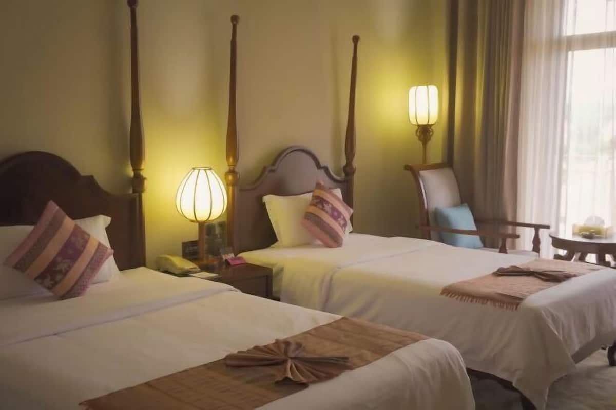 Una habitación de hotel con dos camas, una mesita de noche con lámpara, una silla y una pequeña mesa.