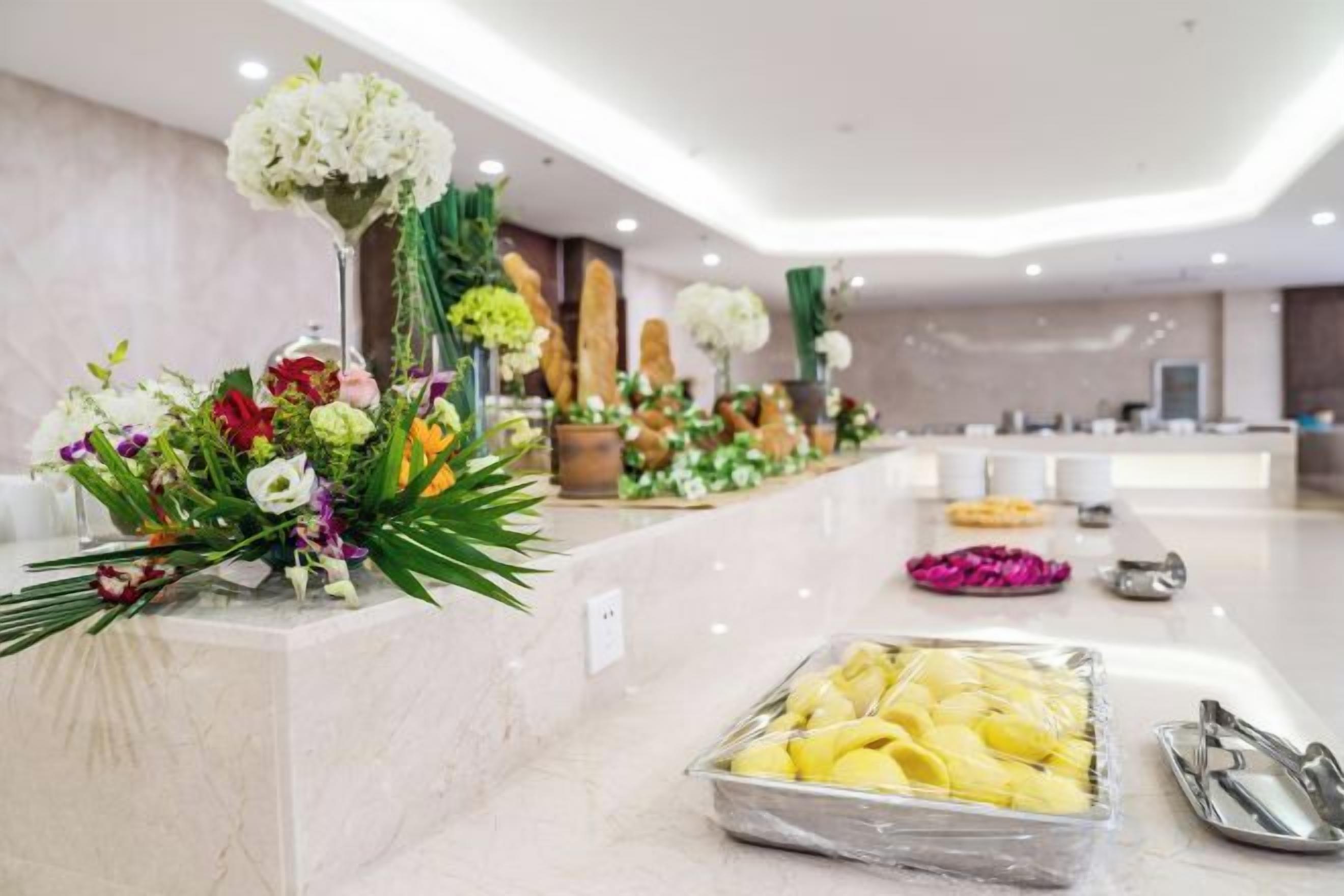 A hotel reception area with a marble counter, floral arrangements, and a buffet with yellow items.