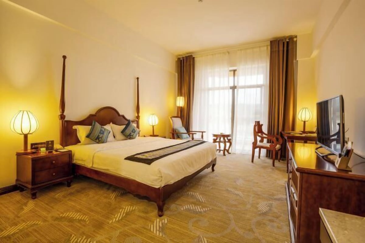 A hotel room with a large bed, bedside lamps, a desk with a television, and a chair.