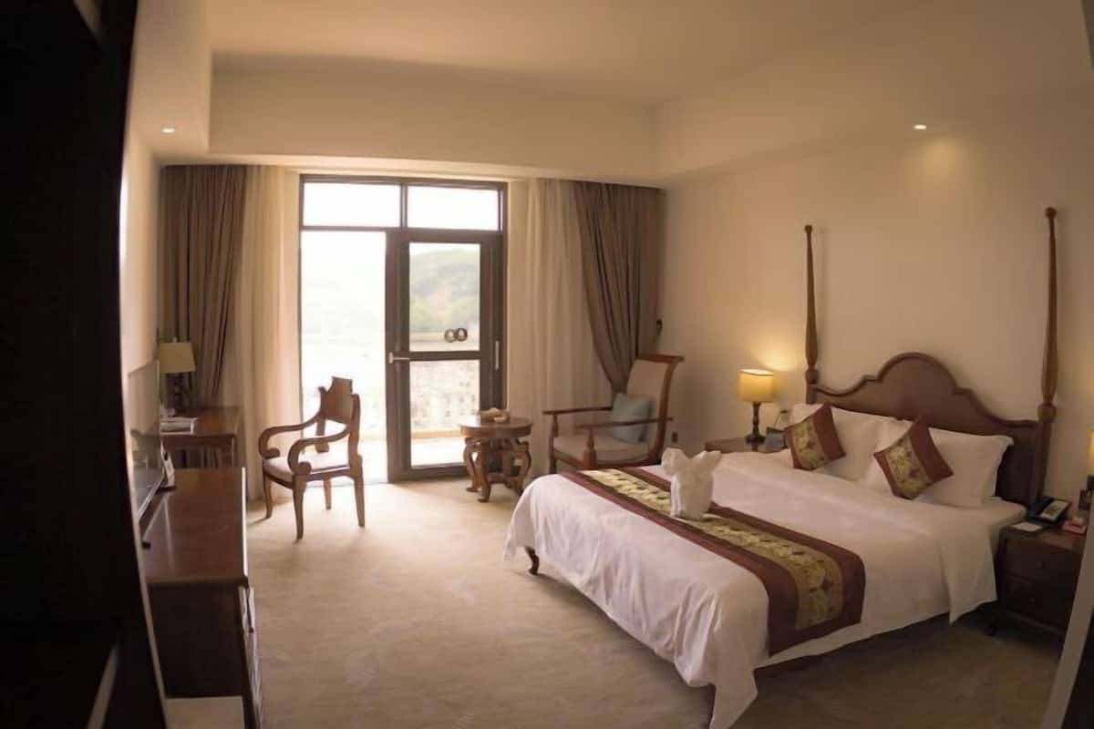 Habitación de hotel con una cama grande, un escritorio, una silla y vistas amplias por una ventana grande.