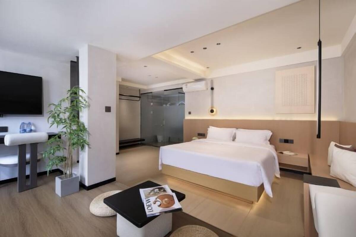 Ein modernes Hotelzimmer mit Bett, Nachttischen, Fernseher und einer Pflanze.