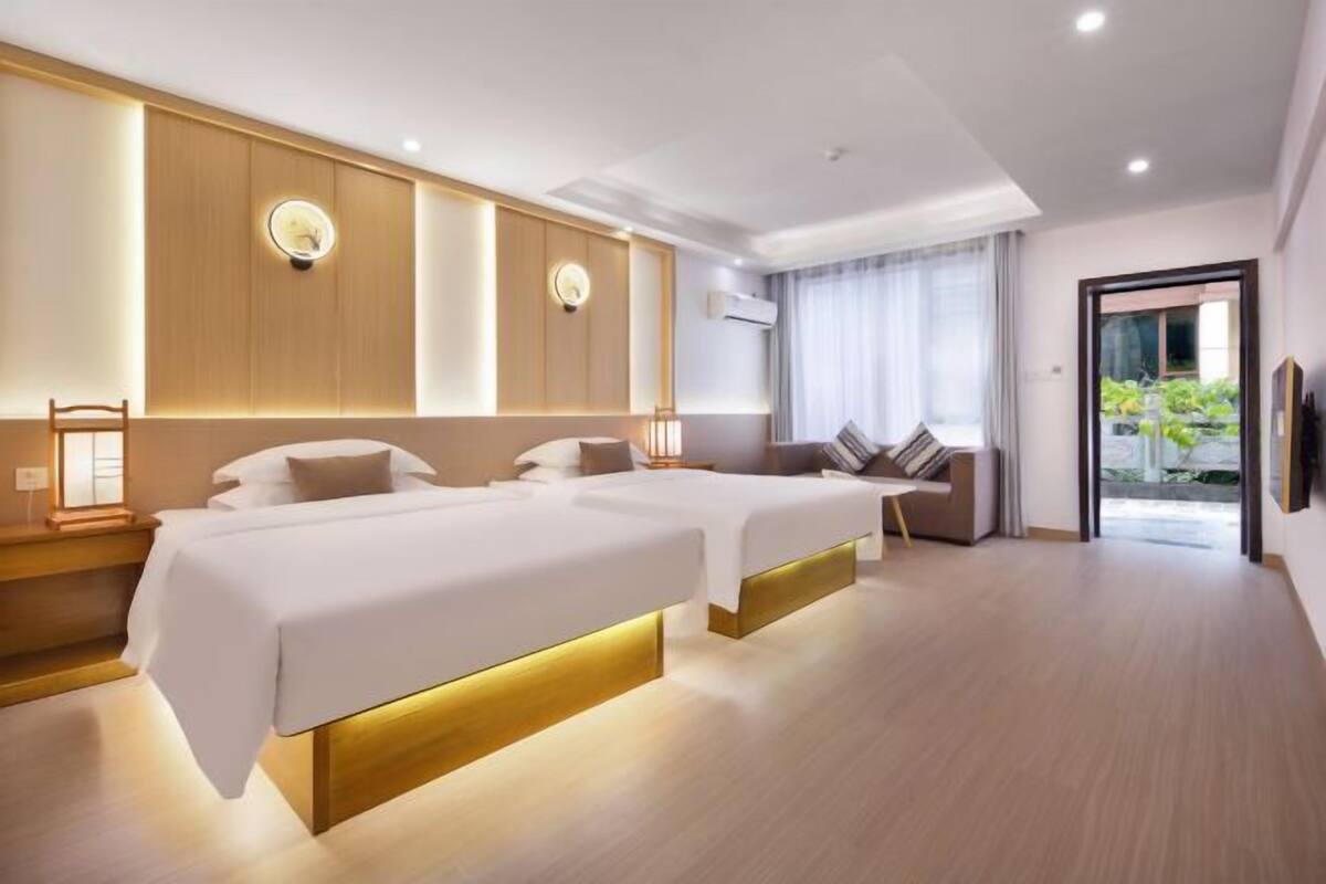 Ein modernes Hotelzimmer mit zwei Betten, einem Sofa und einem großen Fenster mit Vorhängen.