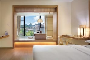 Habitación de hotel con una ventana grande, una mesita de noche, una lámpara y una cama.