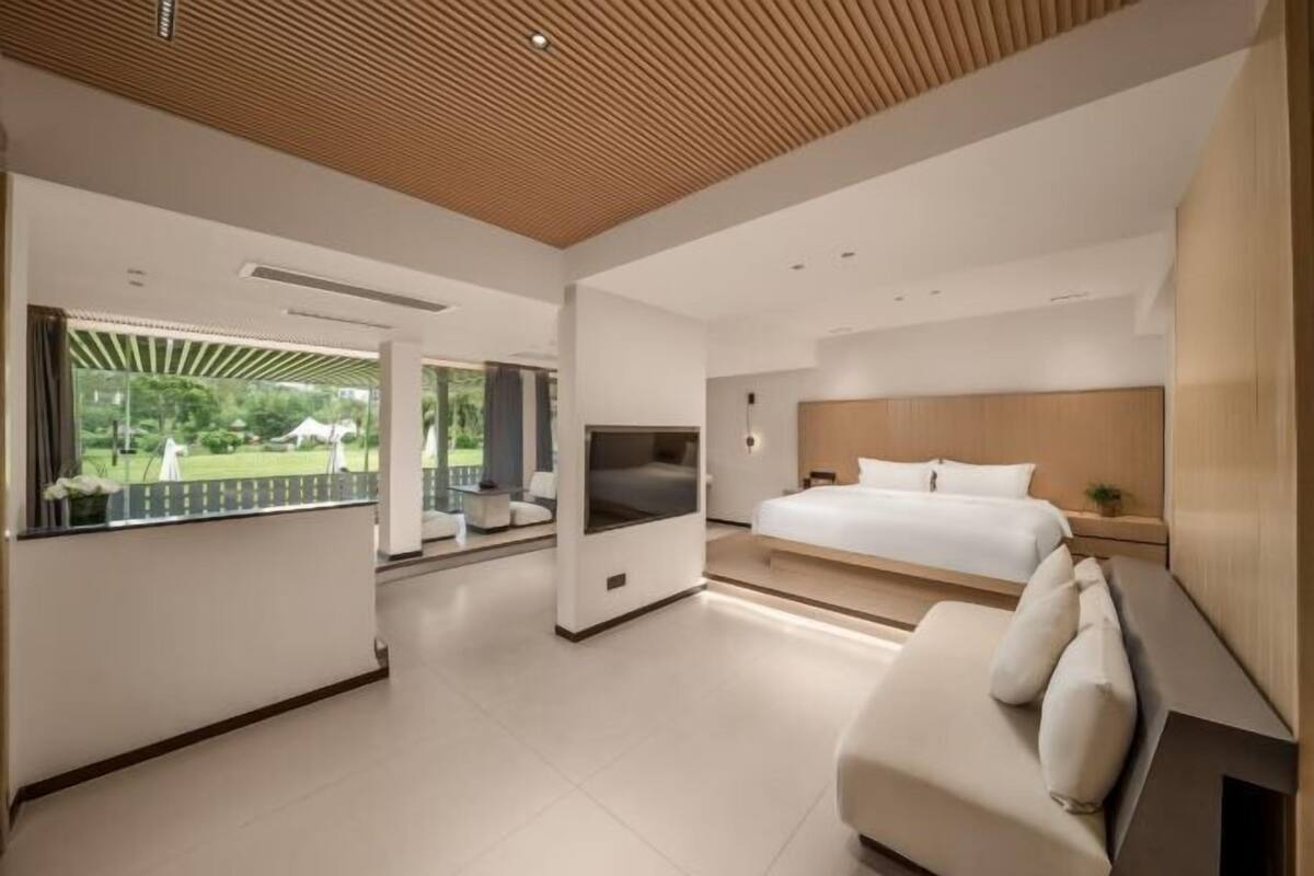 Ein modernes Schlafzimmer mit einem großen Bett, einem Fernseher und einem Balkon mit Blick auf Grünflächen.