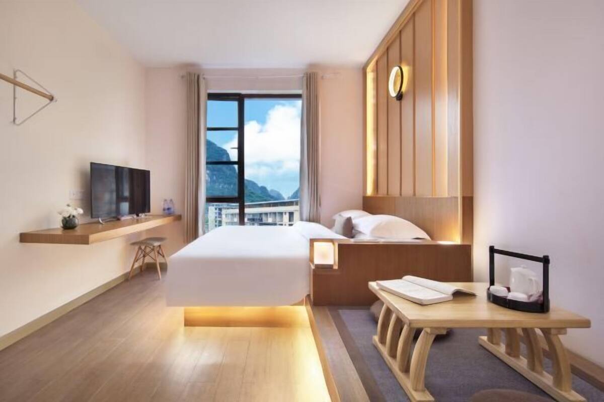 Ein modernes Hotelzimmer mit einem großen Bett, einem Schreibtisch mit Stuhl, einem Fernseher und Bergblick.