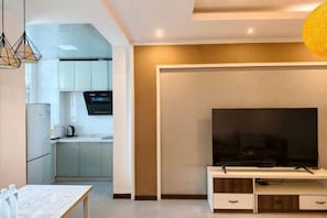 Ein modernes Wohnzimmer mit Flachbildfernseher, einem Esstisch und einer Küchenzeile im Hintergrund.
