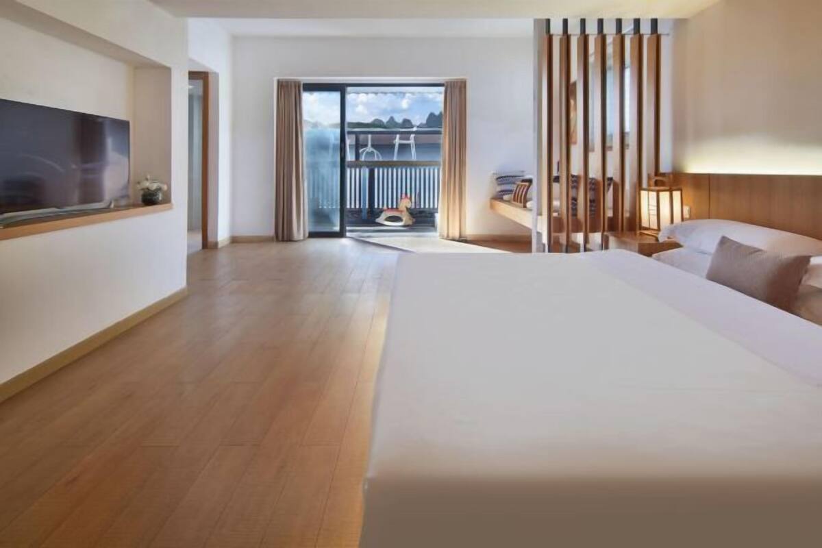 Ein modernes Hotelzimmer mit einem großen Bett, einem an der Wand montierten Fernseher, einem Balkon mit Aussicht und einer Schiebetür zum Außenbereich.