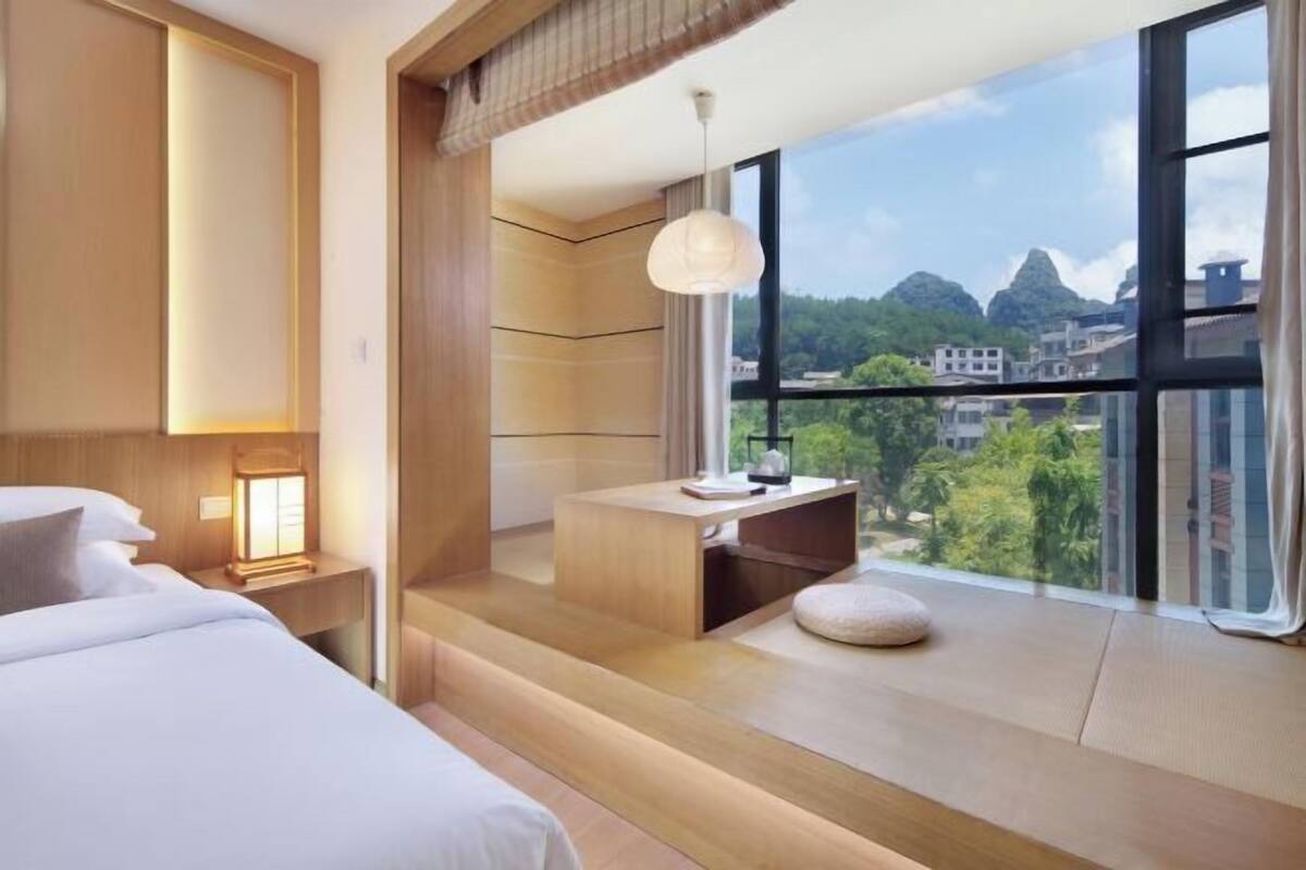 Ein modernes Hotelzimmer mit großem Fenster, einem Bett, einem Schreibtisch und Blick auf die Stadt.