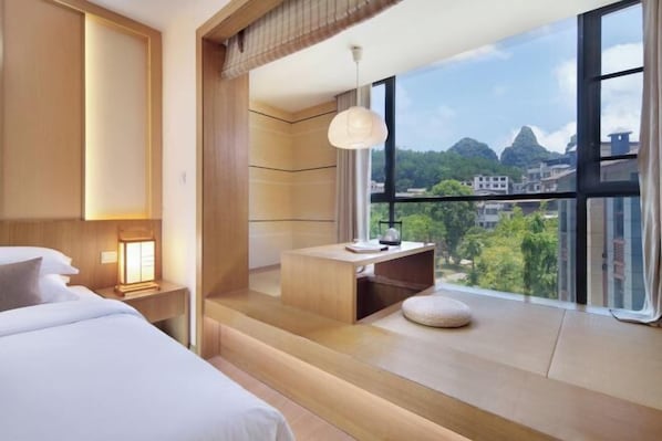 A modern hotel room with a large window, a bed, a desk, and a view of the city. - Panlong Bay Liban Shengjing Hot Spring Resort Hotel (Yangshuo Lijiang) (Yangshuo)