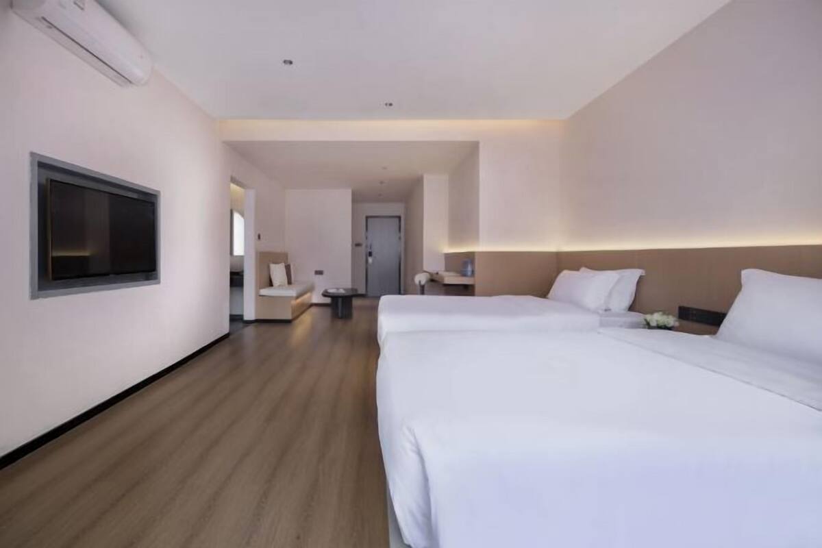 Ein Hotelzimmer mit zwei Betten, einem flachbildfernseher an der Wand und Holzboden.