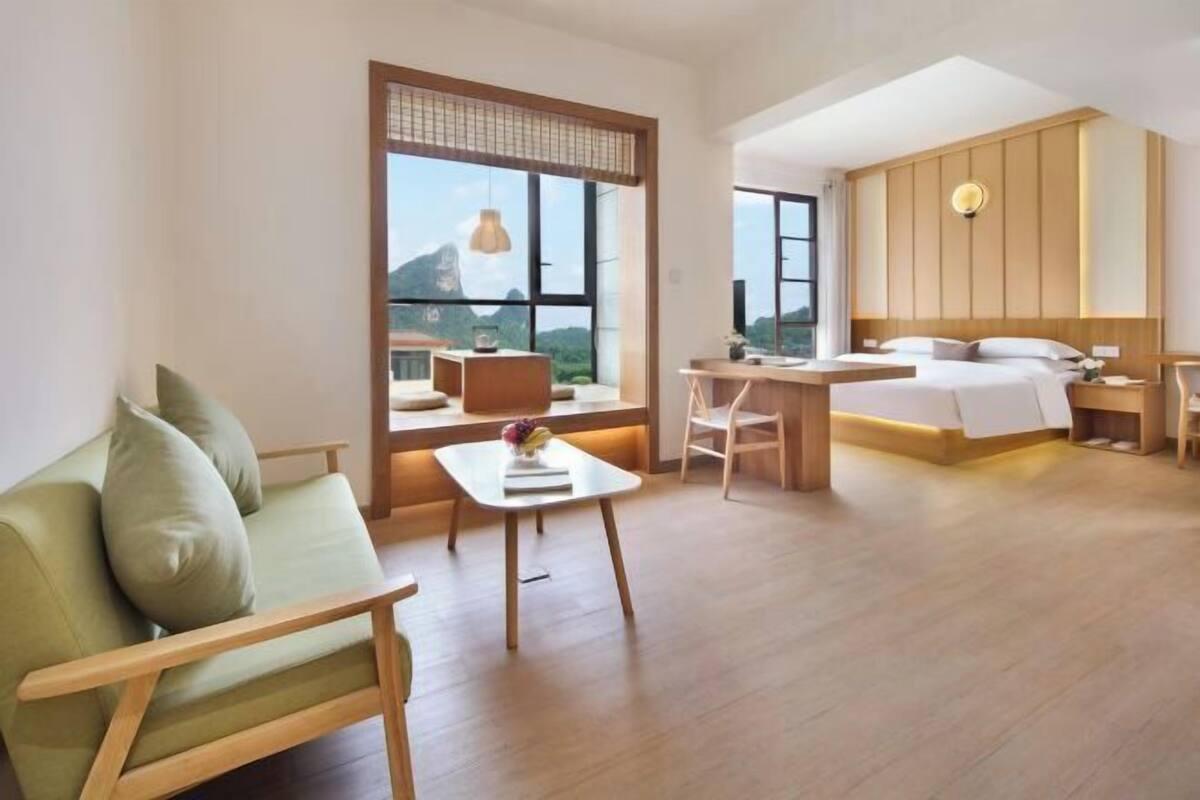 Ein modernes Hotelzimmer mit einem großen Bett, einem Schreibtisch, einer Couch und Blick auf Berge durch große Fenster.